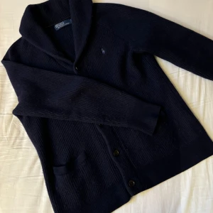 Ralph Lauren Stickad Cardigan - En fet cardigan från Ralph Lauren, är storlek L men sitter mer som M. Har ett litet hål(sista bilden) men syns knappt när man använder den. Hör av er vid eventuella frågor!!