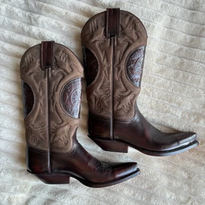 Bruna cowboy boots från Santana - Snygga bruna cowboy boots från Santana med spetsig tå. De är i skinn med en robust klack och detaljerad brodering!