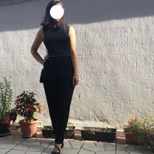Jumpsuit - Snygg svart komplett med glittrig yta och ärmlös design. Perfekt för en kväll ute eller en speciell tillställning. Plagget har en tight passform som framhäver figuren.