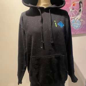 Svart hoodie med blå och gröna detaljer - Snygg svart hoodie med unika blå och gröna grafiska detaljer. Den har en klassisk känguruficka och justerbar huva med dragsko. Perfekt för en avslappnad stil. Priserna går att diskutera!! 