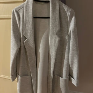 Grå kavaj - Snygg grå kavaj med trekvartsärm och stilren design. Perfekt för en chic och avslappnad look. Kavajen har en öppen front och två fickor framtill.