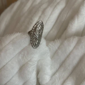 Silverfärgad ring med detaljer - Elegant silverfärgad ring med intrikata detaljer och ett unikt mönster. Perfekt för att ge en stilfull touch till din outfit.