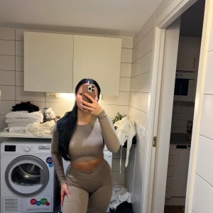 Beige ribbad set med långärmad topp och leggings - Snyggt och bekvämt beige set med ribbad design. Långärmad topp och matchande leggings som ger en tight passform. Perfekt för en stilren look.