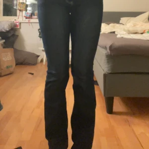 Mörkblå jeans med broderad bakficka - Snygga mörkblå jeans med en unik broderad design på bakfickan. De har en klassisk femficksmodell och en knappgylf. Perfekta för en stilren look. Har spretat upp där nere. 