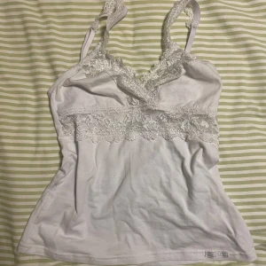 Vitt linne med spets - Säljer en söt vit linnetopp med spetsdetaljer och smala axelband. Står ingen storlek men passar mig som har S och kanske även Xs