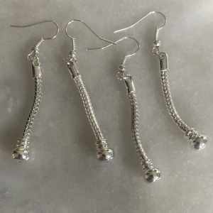 Silvriga örhängen med kedjedetalj - Säljer ett par snygga och stilrena silvriga örhängen med en cool kedjedetalj. De har en lång, smal design med en liten kula längst ner. Perfekta för både vardag och fest! ✨