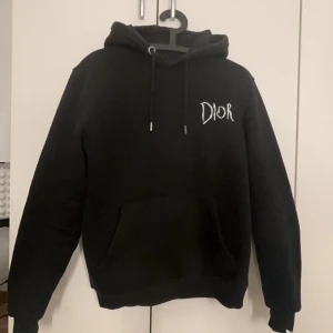 Christian Dior x raymond pettibon hoodie  - Säljer en snygg svart hoodie från Dior. Den har en klassisk design med 'DIOR' broderat på framsidan och 'CHRISTIAN DIOR PARIS' på baksidan. Perfekt för en stilren och avslappnad look. Den är i bra skick och passar perfekt för höst och vinter.