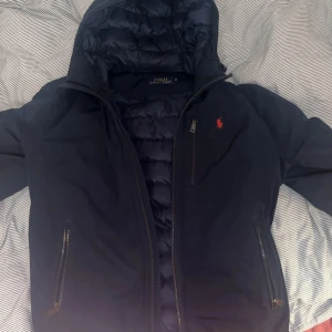 Varm polo ralph lauren höstjacka - Foderad skön Ralph lauren jacka med justerbar luva✅, justerbar midja✅ effektiva fickor med dragkedja samt innerficka✅ Defekt förekommer(lagning på insidan se bild 4) På utsidan är jackan till synes nyskick! Denna mångsidiga snygga jacka är ett KAP!
