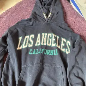 Säljer två hoodies från H&M. Den första är svart med texten 'Los Angeles California' i vitt och grönt. Den andra är grå med en diskret textdetalj i orange. Båda har en klassisk hoodie-stil med ficka fram och är perfekta för en avslappnad look. Passar bra till både höst och vår!