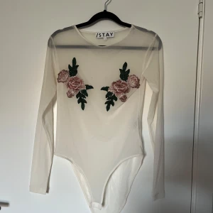 Body - Vit/genomskinlig body med broderade blommor. Använd fåtal gånger. Stretchigt material