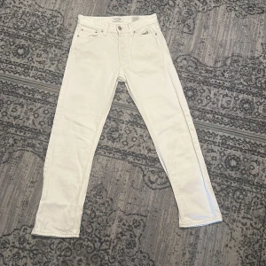 Vita jeans från Jack & Jones - Snygga vita jeans från Jack & Jones med klassisk femficksdesign. De har en rak passform och är perfekta för en stilren look. Byxorna har en knappgylf och är tillverkade i ett slitstarkt material.