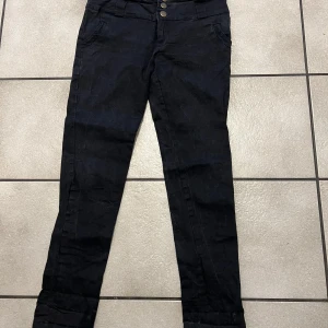 Svarta byxor med knappar midja 72 cm - Snygga svarta byxor med tre knappar i midjan. De har en klassisk design med fickor fram och bälteshällor. Perfekta för en stilren look.