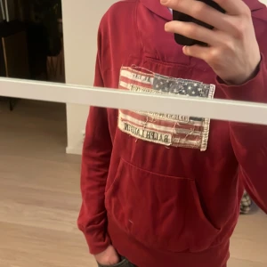Röd hoodie från Ralph Lauren - Säljer en snygg röd hoodie från Ralph Lauren med en amerikansk flagga på bröstet. Tröjan har en klassisk känguruficka och långa ärmar. Jag är 185 på bilden storlek s