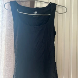 Svart ärmlös topp från lager 157 - Säljer en stilren svart ärmlös topp från 157. Perfekt för varma dagar eller som lager under andra plagg. Toppen har en enkel design med djup rund halsringning. Köparen står för frakten! Pris kan diskuteras💖