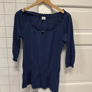 Blå topp från Esprit - Säljer en blå topp från Esprit med trekvartsärmar och volangdetaljer vid halsringningen. Toppen har en elastisk midja som ger en fin passform. Perfekt i vardagen💙