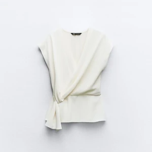 Vit omlottopp från Zara - Elegant vit omlottopp från Zara med knytning i sidan. Toppen har en stilren design med korta ärmar. Säljer då den tyvärr inte kommer till användning❤️kan fixa fler bilder, skriv vid frågor och funderingar