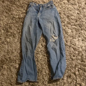 Blå jeans från H&M - Säljer ett par blå ( ganska baggy) jeans från H&M med en cool slitning på ena benet. De har en klassisk femficksdesign och är perfekta för en avslappnad stil. 