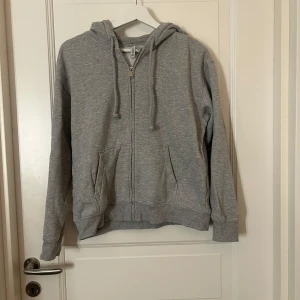 Grå hoodie från H&M - Säljer en basic grå hoodie från H&M. Den har en dragkedja framtill och en mysig huva med dragsko. 