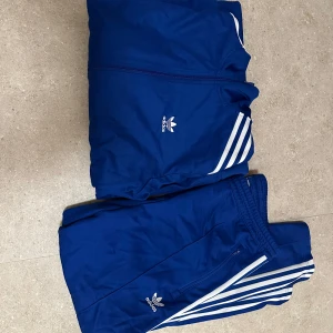 Blå träningsjacka från Adidas - Säljer ett klassisk adidas sett som är i nyskick. Aldrig andvänt, inhandlat i sthlm förra sommaren. Ger en cool look och passar både som tränings kläder eller vardags kläder! Handla dig en riktig sommar outfit!