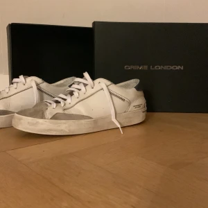 Vita sneakers från Crime London - Snygga vita sneakers från Crime London med grå detaljer och snörning. Perfekta för en stilren look. Skorna har en modern design med en bekväm passform. Kan passa 43!
