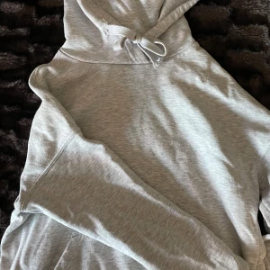 Grå hoodie med ficka - Säljer en stilren grå hoodie med känguruficka och justerbar huva. Perfekt för en avslappnad look. Passar bra till både jeans och mjukisbyxor. Hör av dig vid intresse!