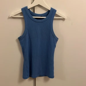 Blå ribbad linnetopp från KappAhl - Säljer en snygg blå ribbad linnetopp från KappAhl. Toppen är ärmlös och har en rund halsringning, perfekt för varma dagar. Den är i storlek XS och passar utmärkt till både jeans och kjol.