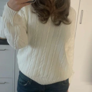 Vit stickad tröja från brandy - Säljer en stilren vit stickad tröja med kabelstickat mönster. Tröjan har en v-ringad hals och långa ärmar, perfekt för kyligare dagar. Passar bra till jeans för en avslappnad look.
