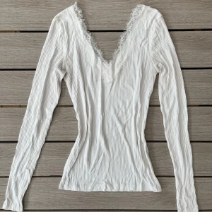 Vit ribbad topp med spetsdetaljer - Säljer denna fina vita ribbade topp med v-ringning och spetsdetaljer i storlek XS💓