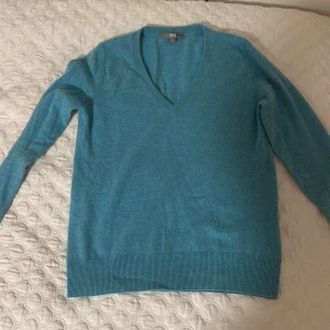Turkos kashmirtröja från Uniqlo - Säljer en mjuk och stilren turkos kashmirtröja från Uniqlo. Tröjan har en v-ringad design och långa ärmar, perfekt för kyligare dagar. Den är i storlek S och har ribbade kanter för en snygg passform. Ett litet hål där fram som knappt syns, därav säljer jag billigt. Perfekt för att hålla sig varm och bekväm.
