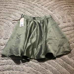 Grön kjol från Bubbleroom - Snygg grön kjol från Bubbleroom i en glansig finish. Kjolen har en vid passform och är kort i modellen, perfekt för en trendig look. Den har en dragkedja i sidan för enkel på- och avtagning. Ett stilrent val för den modemedvetna!