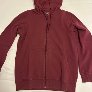 Vinröd hoodie med dragkedja - Säljer en vinröd hoodie med dragkedja och huva. Tröjan har långa ärmar och praktiska fickor framtill. Perfekt för en avslappnad stil. Skicket är 8/10. (Pris kan diskuteras vid snabb affär) 😃