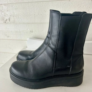 Svarta boots från Vagabond - Snygga svarta boots från Vagabond i skinn med en robust sula. De har en stilren design utan snörning och är perfekta för både höst och vinter. Enkla att dra på tack vare resårpaneler på sidorna. Lite skav fram på ena skon, se bild 5.