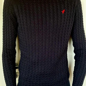 Mörkblå stickad tröja från Pier One - Säljer en snygg mörkblå stickad tröja från Pier One. Den har ett kabelstickat mönster och en liten röd logga på bröstet. Perfekt för både höst och vinter, med långa ärmar och en bekväm passform. Passar till både vardag och lite finare tillfällen. Hör av dig vid frågor!