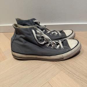 Säljer ett par klassiska grå Converse All Star sneakers i bra skick. De har den ikoniska höga modellen med vita snören och gummisula. Perfekta för vardagsbruk och ger en avslappnad stil. Lite slitna men fortfarande snygga och bekväma.