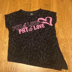 Cool svart t-shirt med leopardmönster och rosa text 'PRT & LOVE' samt ett hjärta. Perfekt för en avslappnad stil med en twist. Kortärmad och i bra skick.