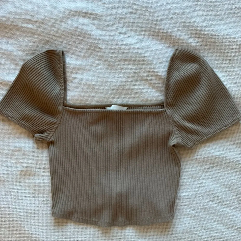 Säljer en superfin beige ribbad topp från H&M. Den har korta puffärmar och en croppad passform som är perfekt för sommaren. Toppen är i mycket bra skick och passar både till vardags och fest. Perfekt att matcha med ett par höga jeans eller en kjol!. Toppar.