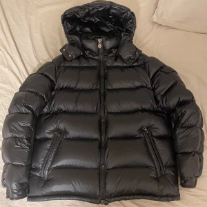 Svart Maya moncler  - Säljer en snygg svart dunjacka från Moncler i mycket bra skick. Jackan har en pufferstil med en praktisk huva och dragkedja framtill. Perfekt för kalla vinterdagar! Den är både varm och stilren, med Monclers ikoniska logga på ärmen. Passar perfekt för vinterns alla äventyr. Pris kan diskuteras!!