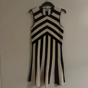 Svart och vit randig klänning - Snygg svart och vit randig klänning i stickat material. Den är ärmlös och har ett coolt geometriskt mönster som verkligen sticker ut. Perfekt för både vardag och festliga tillfällen. Klänningen är i mycket bra skick och har en skön passform som är normal.