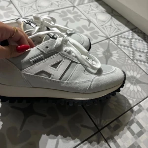 Vita sneakers från Axel Arigato - Säljer ett par snygga vita sneakers från Axel Arigato i mycket bra skick. De har en stilren design med snörning och en bekväm sula. Perfekta för både vardag och fest! 🏃‍♂️✨