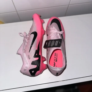 Nike Zoom Mercurial fotbollsskor - Säljer ett par grymma Nike Zoom Mercurial fotbollsskor i en snygg rosa färg med svarta detaljer. Skorna har snörning och är i nytt skick. Perfekta för fotbollssäsongen och ger dig den där extra farten på planen! Storlek och passform är normal.