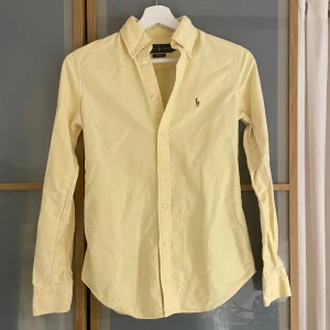Ljusgul skjorta från Ralph Lauren - Säljer en snygg gul skjorta från Ralph Lauren i storlek XS. Skjortan har en klassisk design med knappar och en broderad logga på bröstet. Perfekt för både vardag och fest! 💛