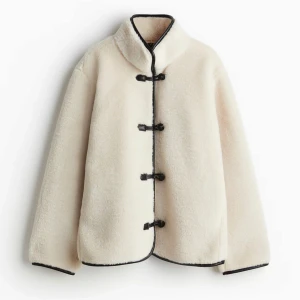 Beige teddyjacka med svarta detaljer - Säljer en supermysig beige teddyjacka med svarta knappar och kantdetaljer. Jackan har en loose passform och är perfekt för höst och vinter. Den är långärmad och gjord i ett mjukt material som håller dig varm och stilren. Perfekt för både vardag och fest! ÄR SLUTSÅLD ÖVERALLT💘💘💘