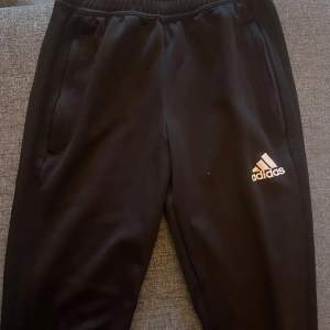 Säljer ett par svarta träningsbyxor från Adidas i bra skick. De har en bekväm passform med elastisk midja och dragkedjor vid bensluten. Perfekta för träning eller en avslappnad dag hemma. Adidas-loggan syns tydligt på benet. Passar till både höst och vinter. (Frakt tillkommer vid köp under 200kr)