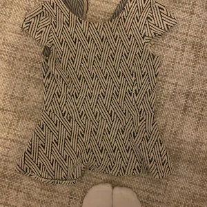 Mönstrad kortärmad tröja  - Säljer en superfin kortärmad tröja med ett unikt geometriskt mönster i svart och beige/vit. Tröjan har en omlott-design baktill som ger en snygg detalj. Perfekt för både vardag och fest!