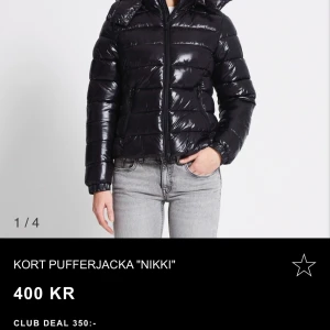 Kort svart pufferjacka 'Nikki' - Säljer en snygg och glansig kort svart pufferjacka 'Nikki'. Perfekt för kyliga dagar med sin varma vaddering och praktiska huva. Jackan har en dragkedja framtill och långa ärmar. Passar perfekt till både vardag och fest! Använd 1-2 ggr. Inga defekter! Storlek M. Säljer eftersom jag har hittat en annan jacka💕