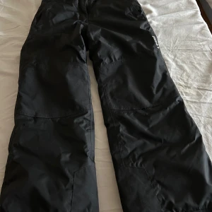 Överdragsbyxor - Svarta för barn - • Märke - Everest  • Storlek - 146 (M/S) • Färg - Svart • Jättebra att ha på sig i snön  och i skidbacken, men även när man åker pulka! • Nytvättad och i mycket bra skick! • Passar perfekt för rasterna i skolan när barnen leker i snön och i regnet