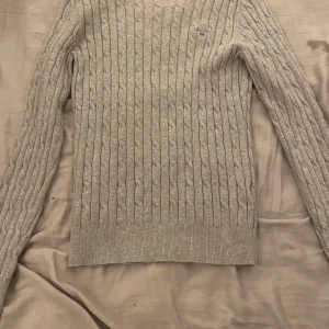 Grå kabelstickad tröja från Gant - Säljer en snygg grå kabelstickad tröja från Gant i stretchig bomull. Perfekt för höst och vinter med sin mysiga och stilrena design. Tröjan har långa ärmar och en liten Gant-logga på bröstet. Passar både till vardags och lite finare tillfällen. Har använts ett fått tal gånger.