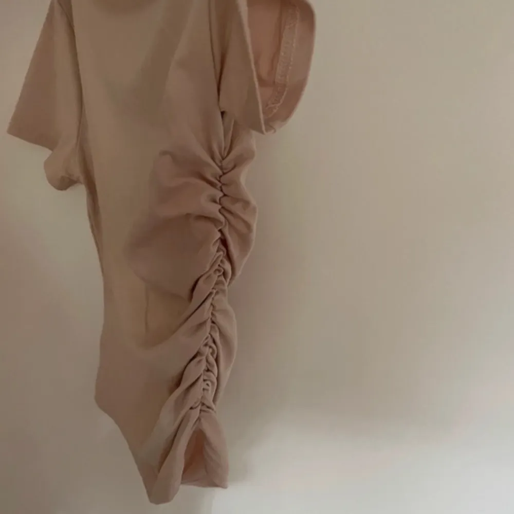 Säljer en snygg beige offshoulder topp med korta ärmar. Toppen har en cool rynkad detalj på sidan som ger den en unik look. . Yläosat.