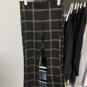 Svarta rutiga byxor från MyWear - Snygga svarta byxor med ett stilrent rutmönster i beige och grått från MyWear. Perfekta för både vardag och fest! De har en rak passform och är superbekväma att bära. Passar perfekt till en enkel topp eller en dressad skjorta.
