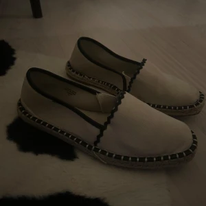 Beige espadrillos med svarta detaljer - Snygga och bekväma beige espadrillos med svarta kanter och detaljer. Perfekta för sommaren med en stilren design och flätad sula. De är lätta att matcha med olika outfits och passar både till vardags och fest.